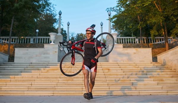 Young and energetic cyclist in the park. Man climbs the stairs holding a bike on his shoulder